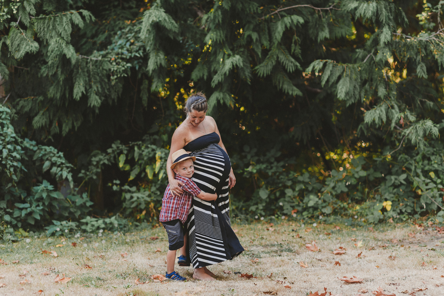  young child hugging his pregnant mother’s legs both smilling-hornby island lifestyle maternity session