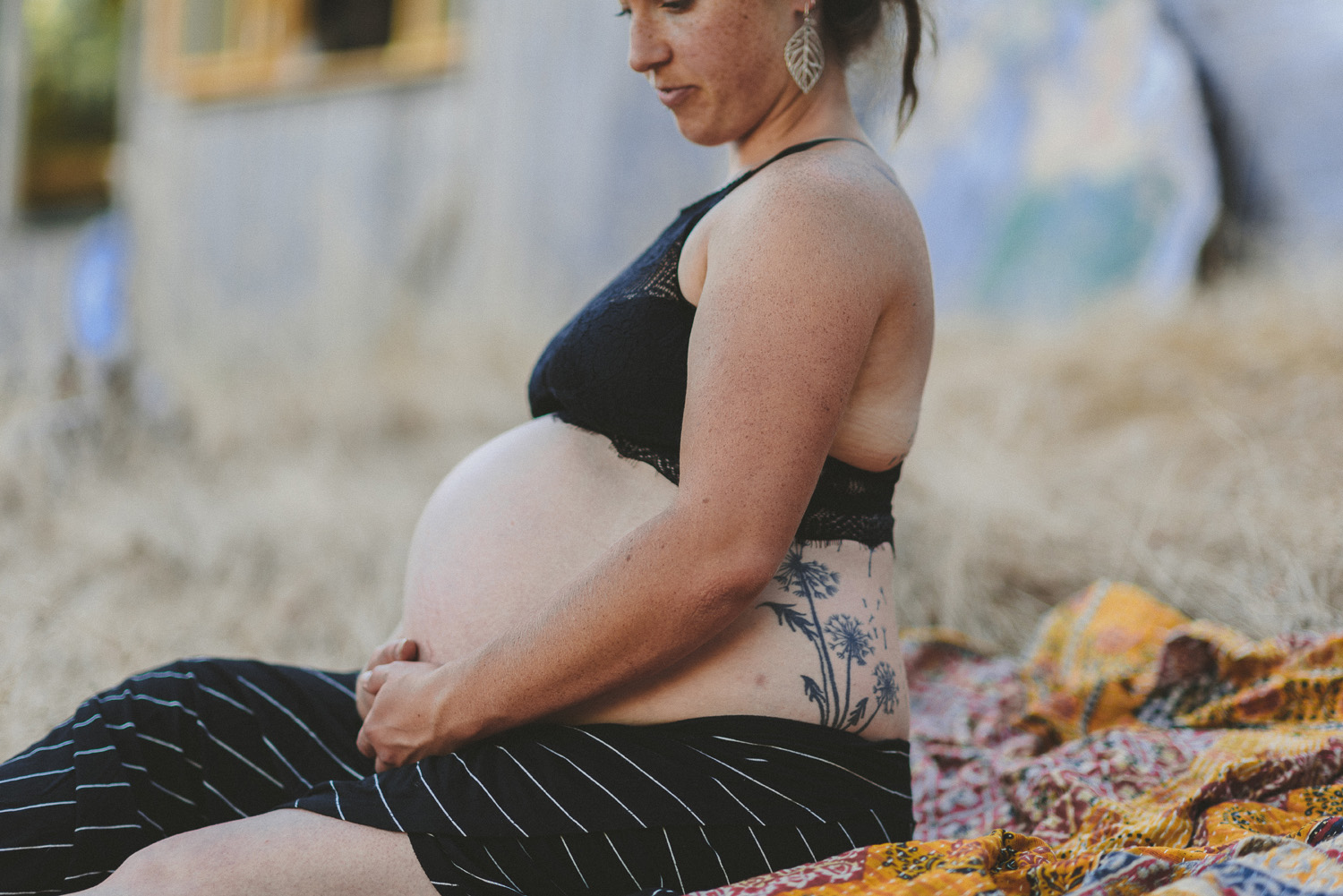 young pregnant woman sitting holder her belly with a dandelion tattoo on her side-hornby island lifestyle maternity session