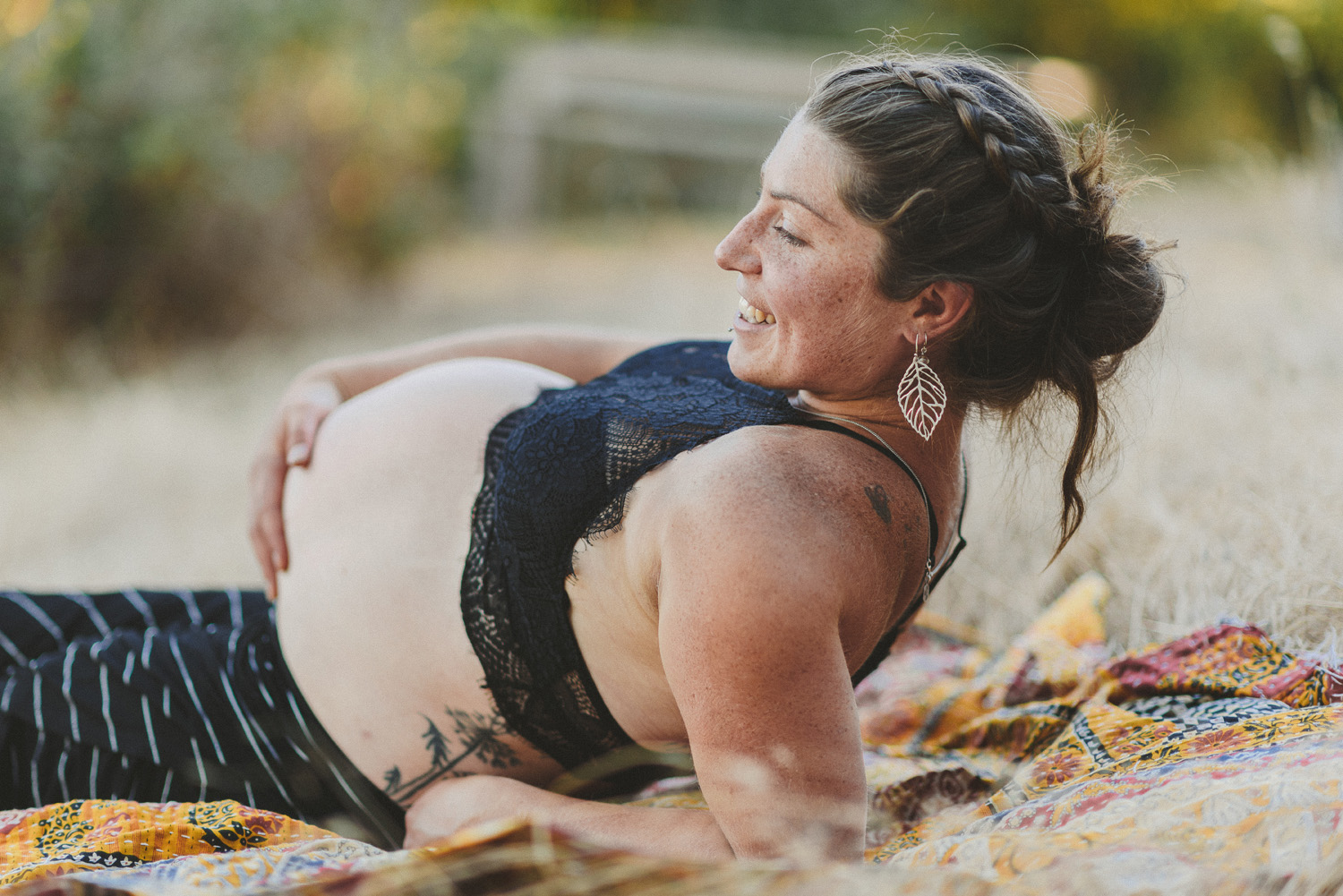 young happy pregnant woman holding her belly reclining on a blanket in the dry grass-hornby island lifestyle maternity session