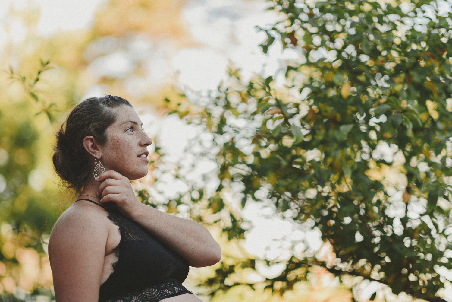 young woman looking upwards holding her feather earing-hornby island lifestyle maternity session