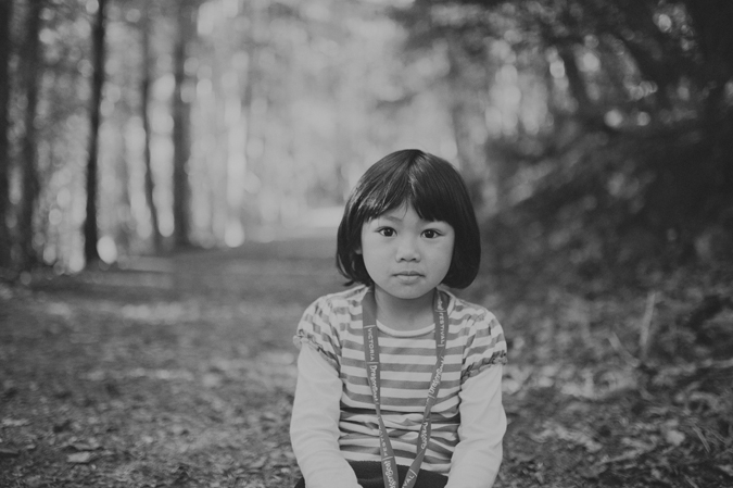 creative black and white photograph of a young girl sitting in the forest staring at the camera on salt spring island, bc