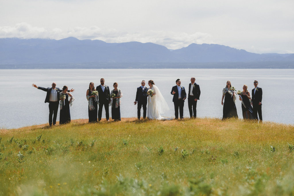 wedding party all laughing on a meadow overlooking the ocean