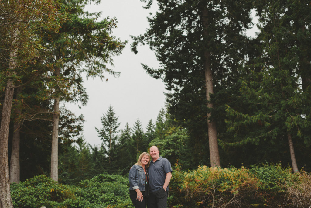 couple hugging in front of tall trees on hornby island