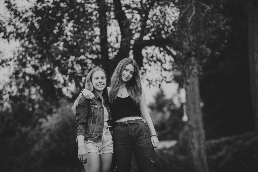 black & white photo of young sisters smiling in front of trees