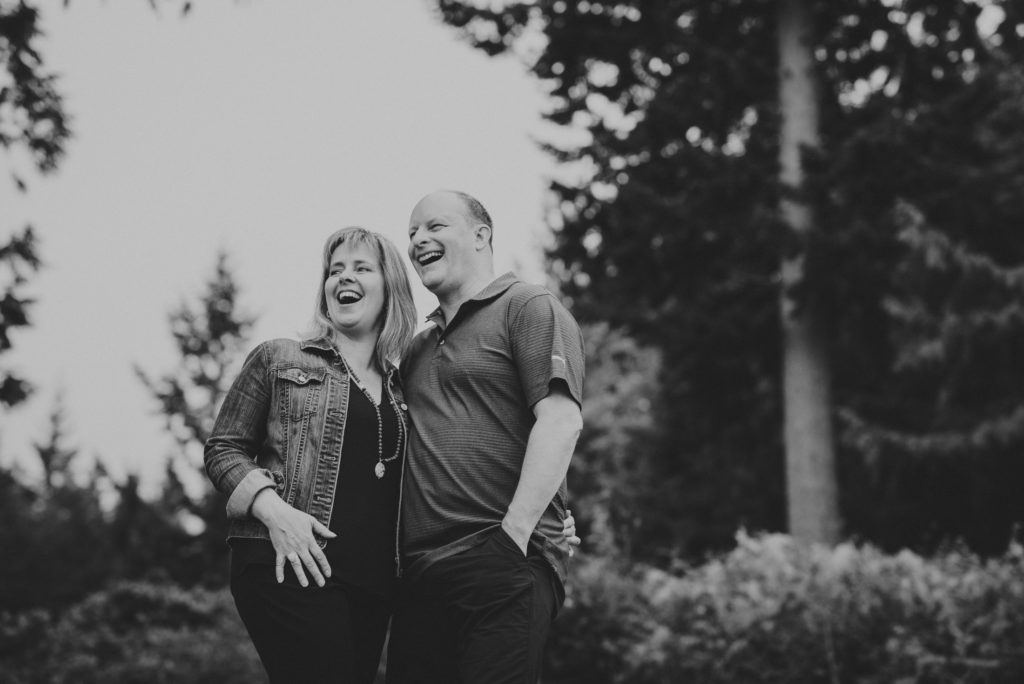 black & white photo of couple laughing with forest behind them