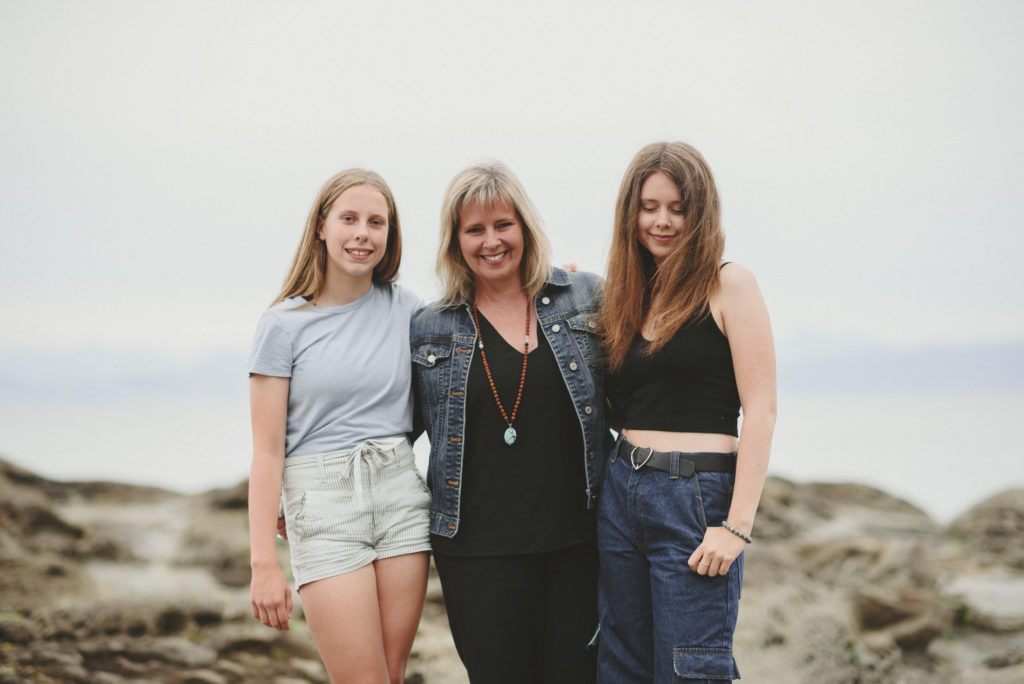 mom & her 2 teenage daughters smiling on the beach
