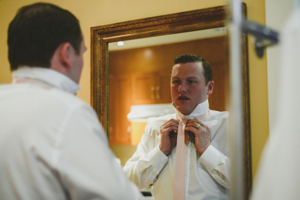 groom tying his tie in a mirror 