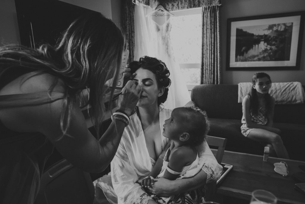 bride holding a child watching her get her make-up put on