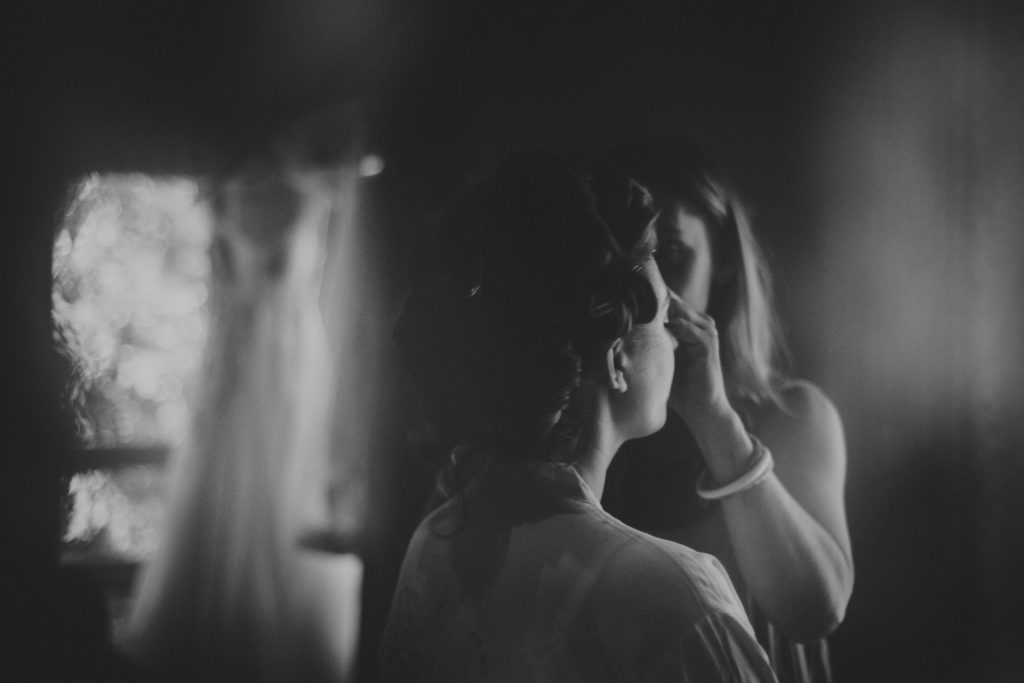 refection of a bride getting her make-up put on with her wedding dress hanging in the background