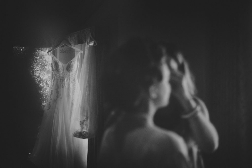 refection of a bride getting her make-up put on with her wedding dress hanging in the background