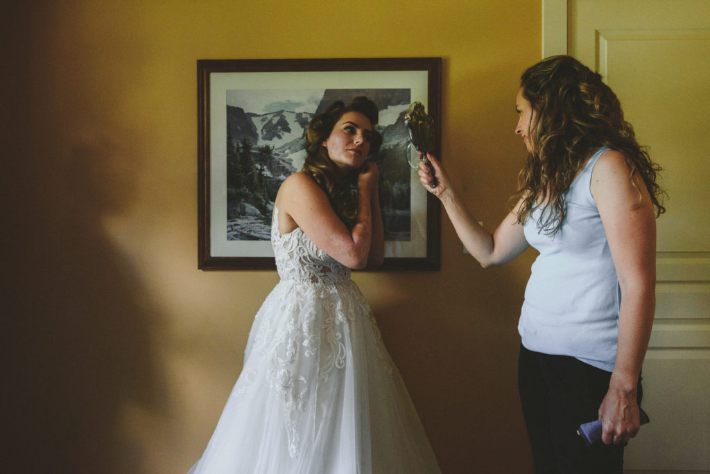 bride's mother holds a mirror while she puts on her wedding day earings