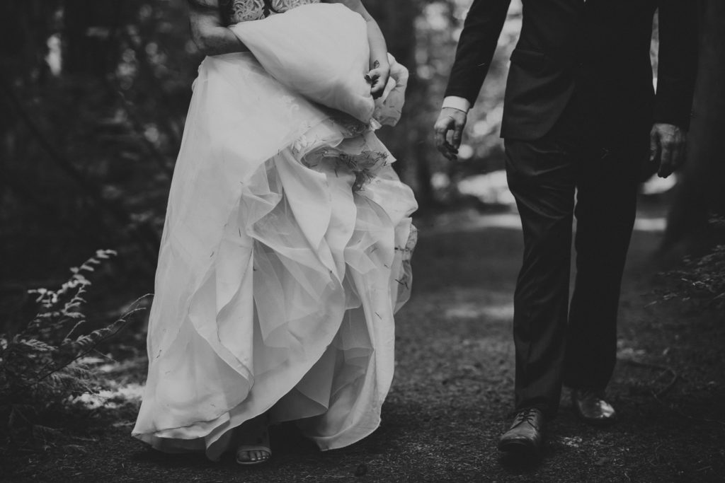 details of bride holding her dress beside her groom in the forest