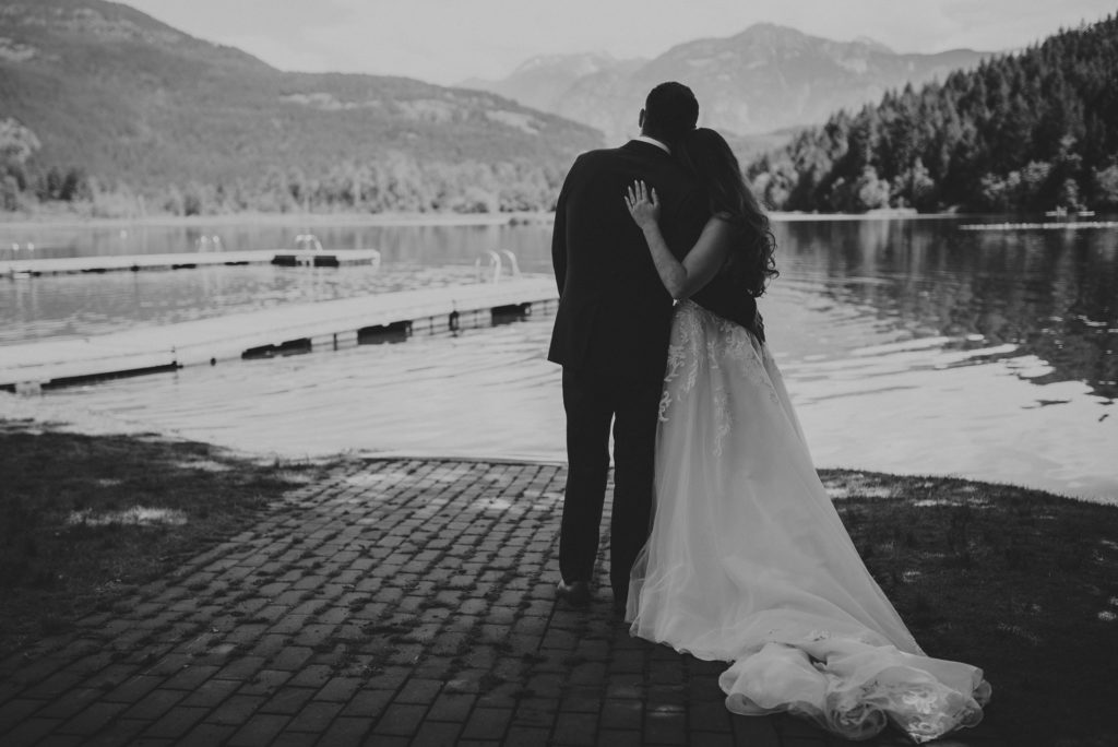 back of bride & groom holding each other with lake & mountains around them