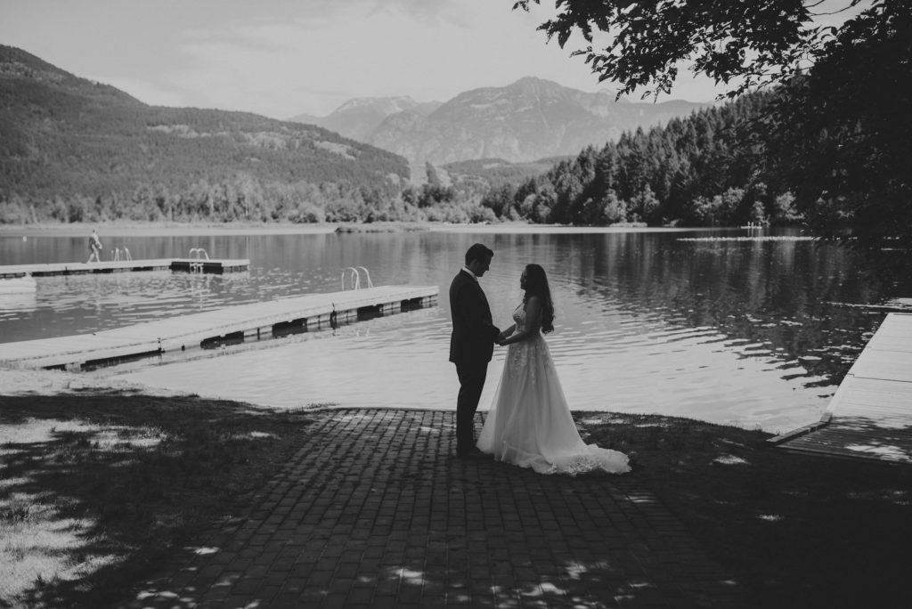 back of bride & groom holding each other with lake & mountains around them