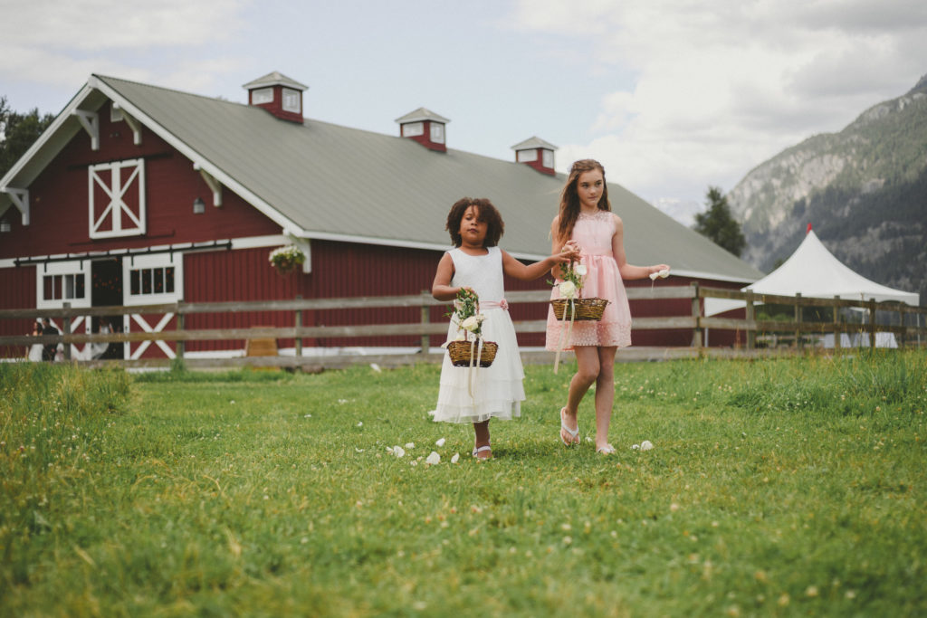 flower girls walking up the aisle with a large red barn behind them