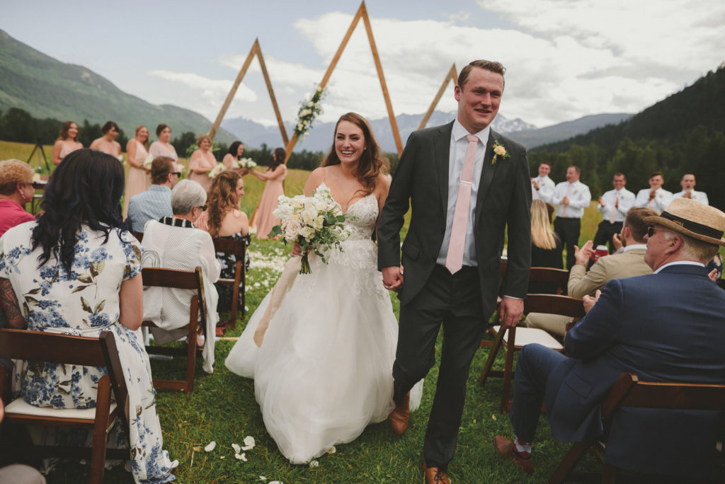 smiling bride & groom walking up the aisle after getting married with the mountains behind them