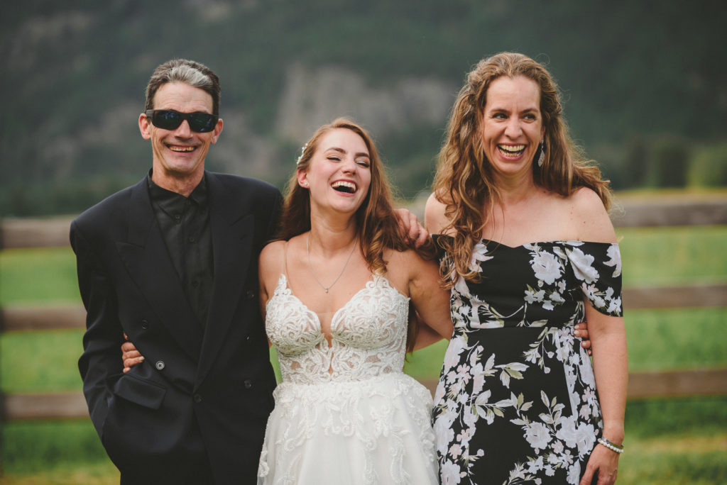 bride & her parents laughing with their arms around one another