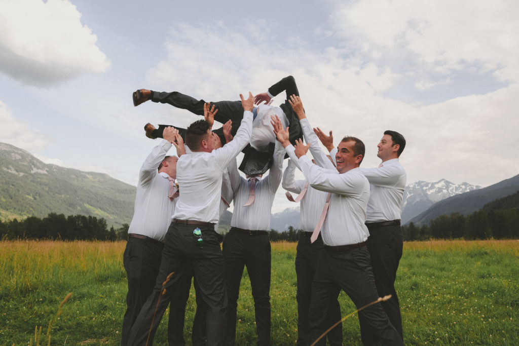 groomsmen picking up the groom with mountains behind them