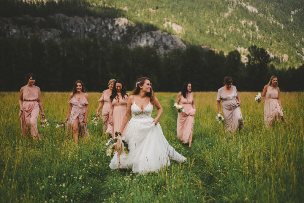bride & bridesmaids walking in a field with mountains behind them