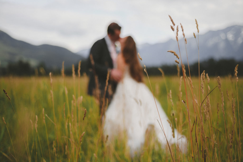 bride & groom kissing in a field with the mountains behind them
