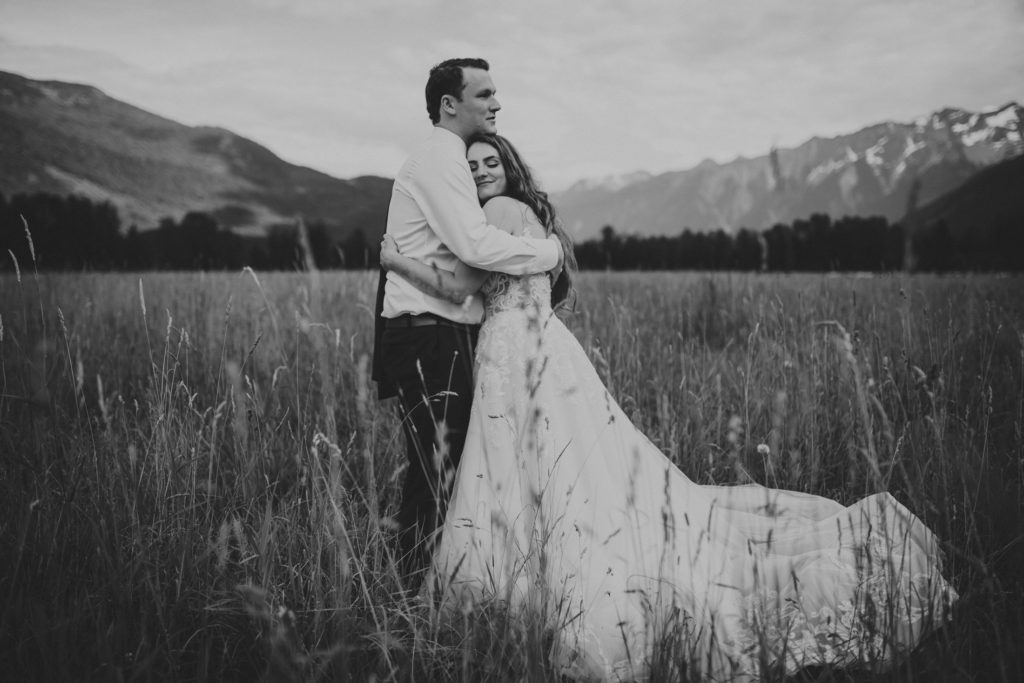 bride & groom hugging in a field with the mountains behind them