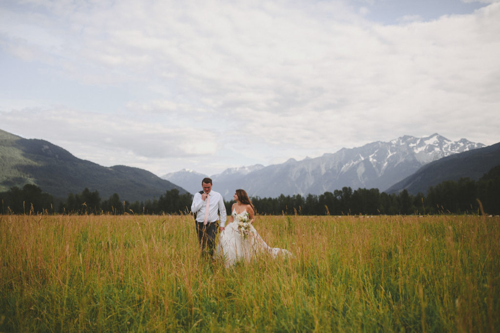 bride & groom walking in a field with the mountains behind them
