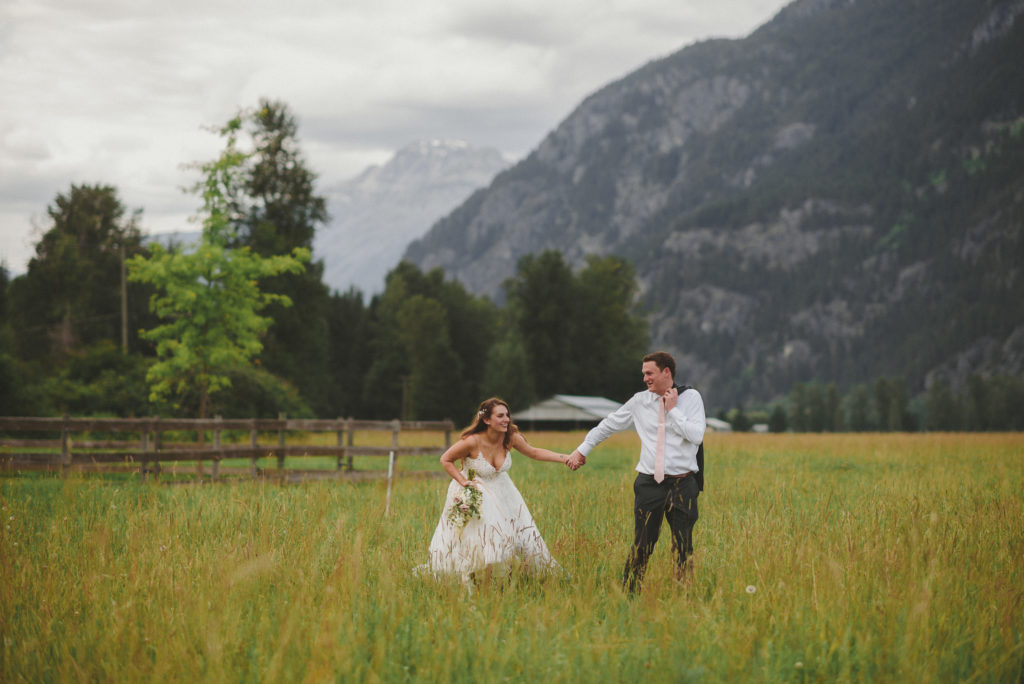 bride & groom walking & laughing in a field with the mountains behind them