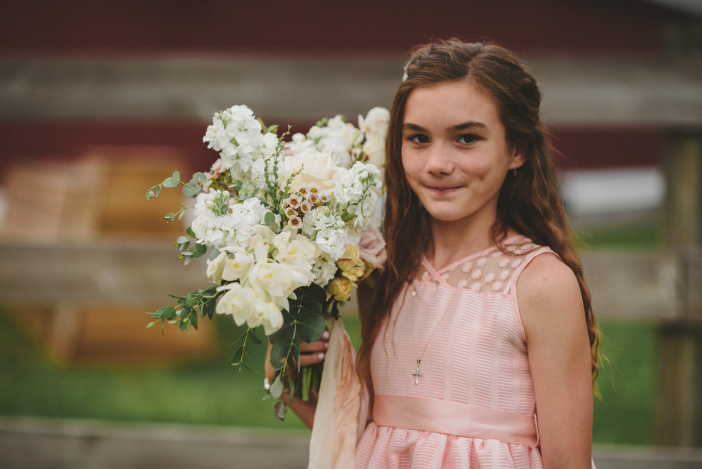 close up of a flower girls smiling at the camera holding a bouquet of flowers