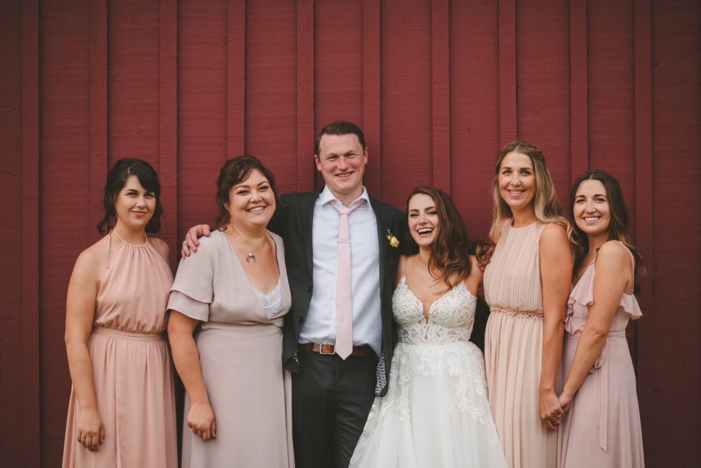 groom & bridesmaids standing against a large red barn