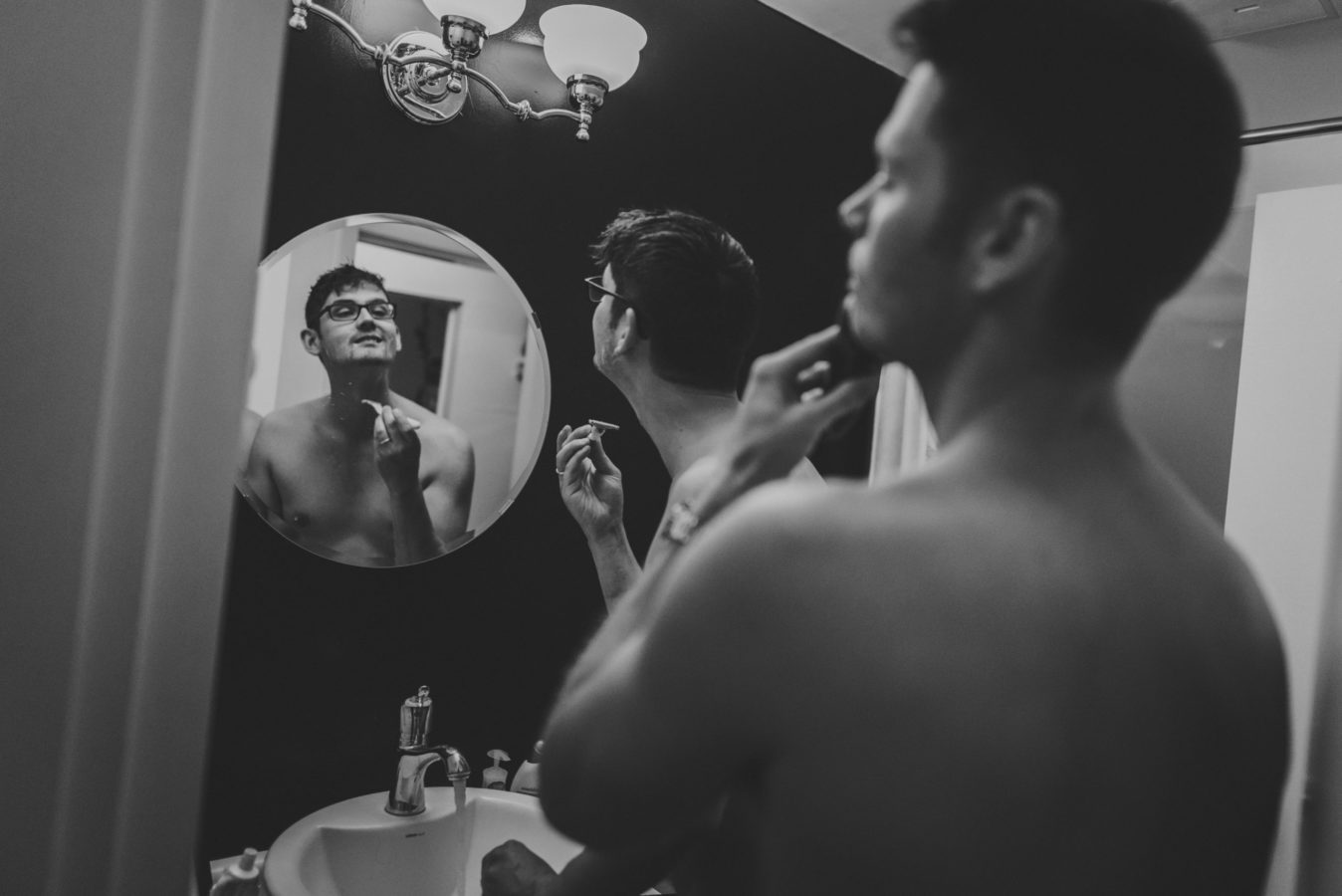 reflection of two men shaving in a bathroom mirror