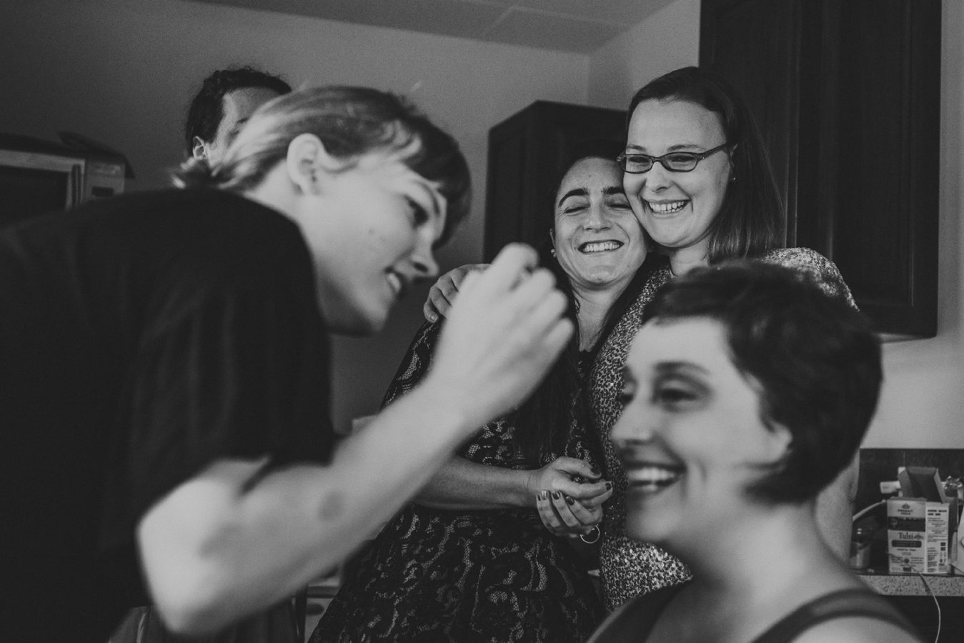 two lgbtq guests hugging and laughing while their friend gets make up done for her wedding