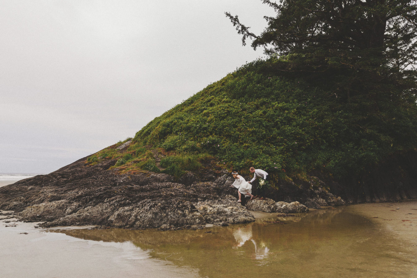 wedding couple climbing on rocks with reflection in the water below