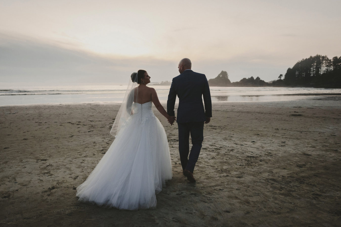 wedding couple holding hands and walking on the sunset beach in tofino