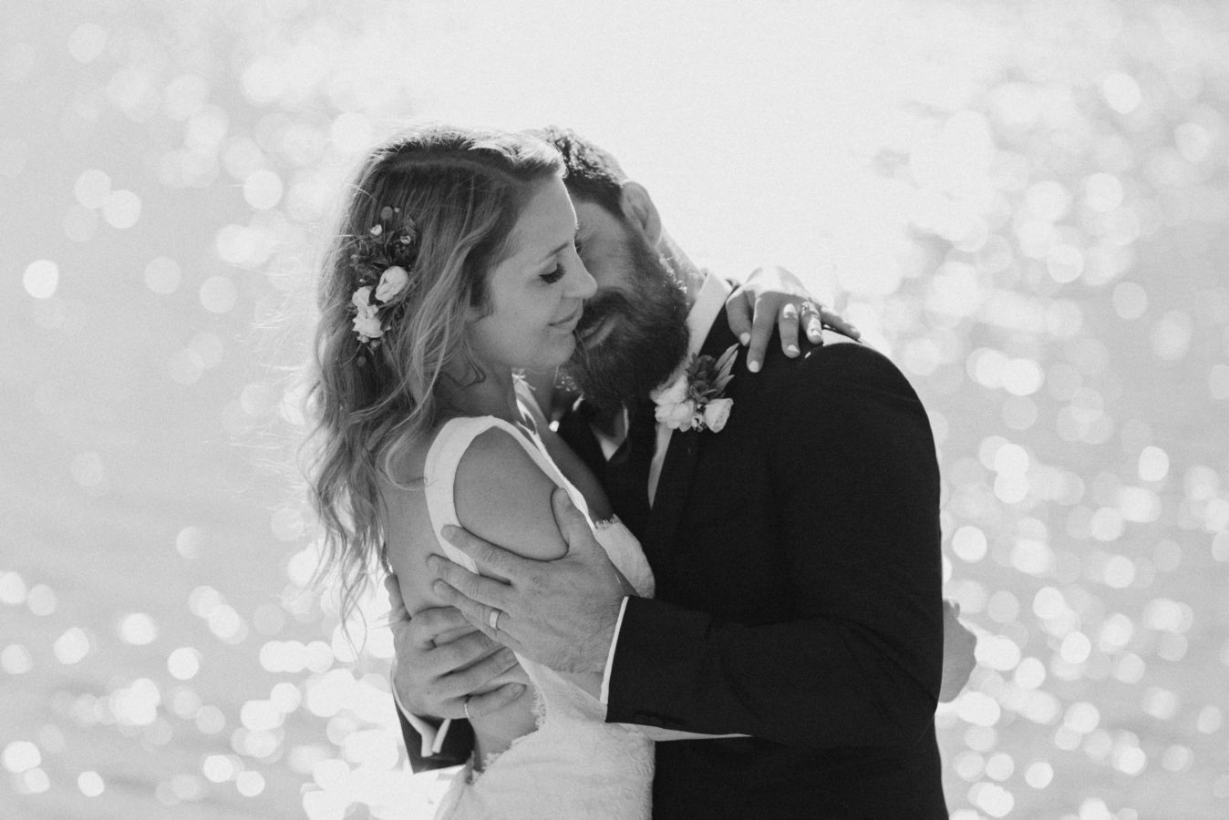 wedding couple embracing with bright sparkly water behind them