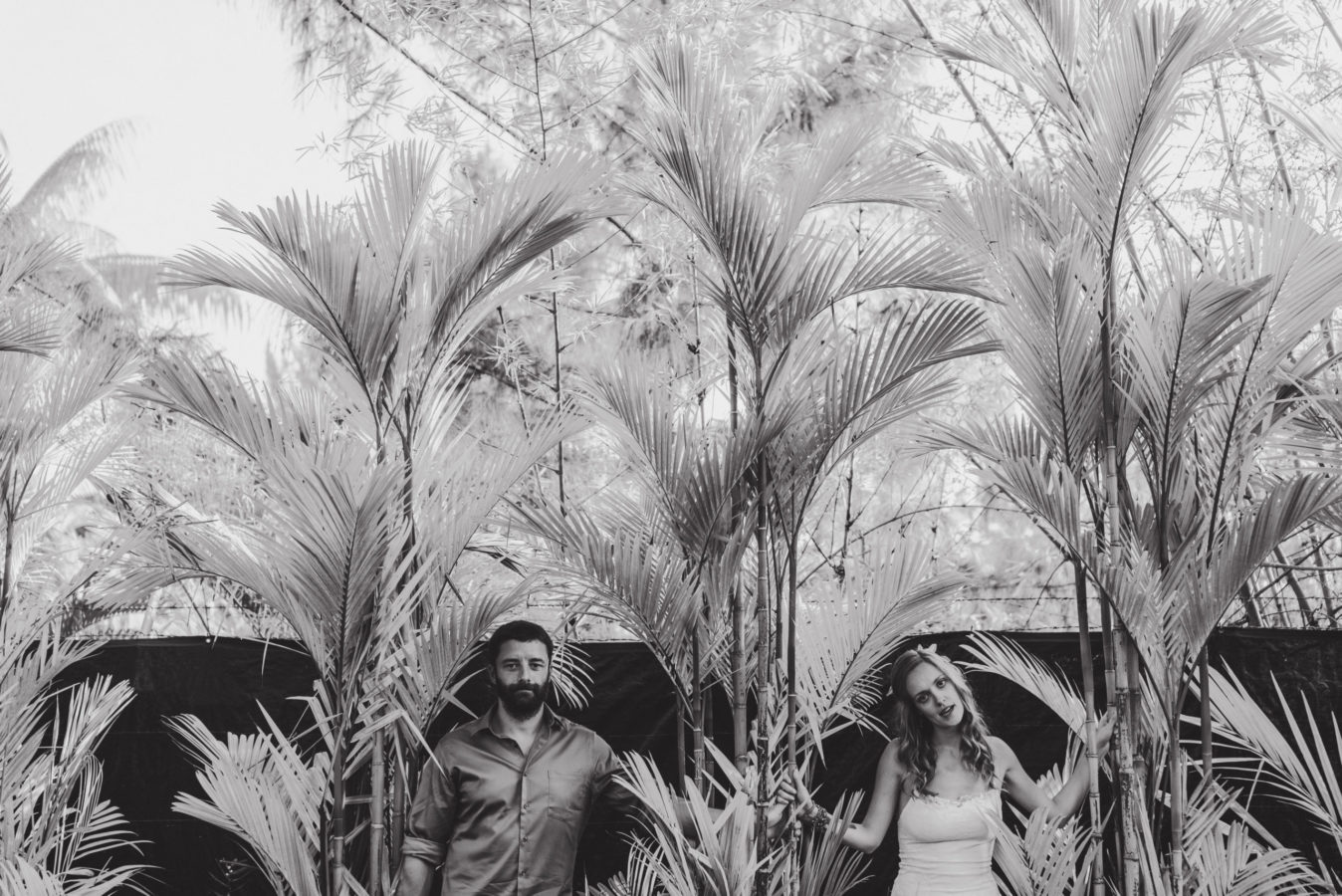 bride and groom standing against a wall amongst palm trees
