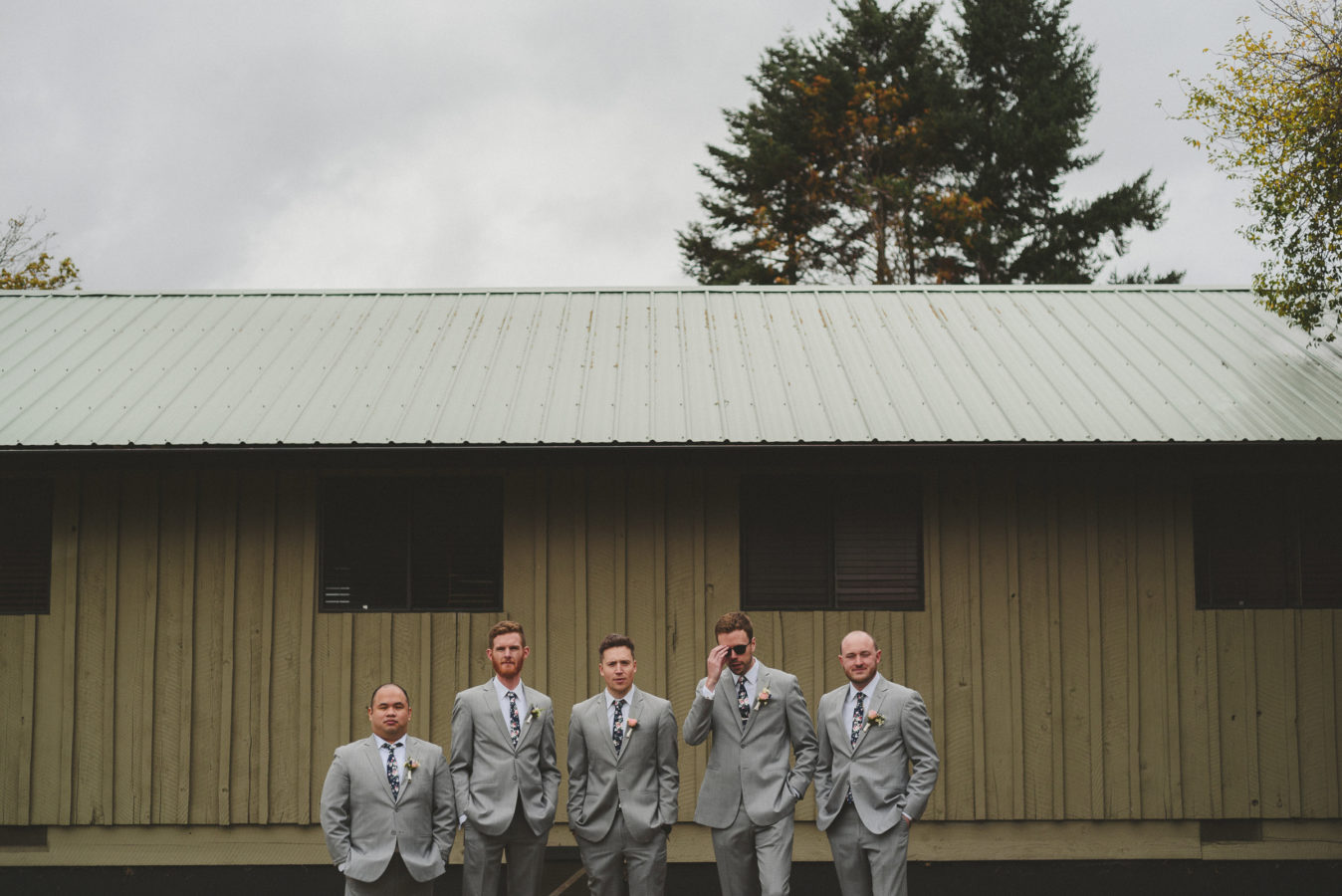 five groomsmen standing and looking at the camera against a rustic cabin