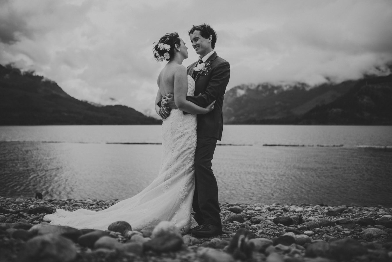young bride and groom embracing in front of a lake & mountains on their wedding day