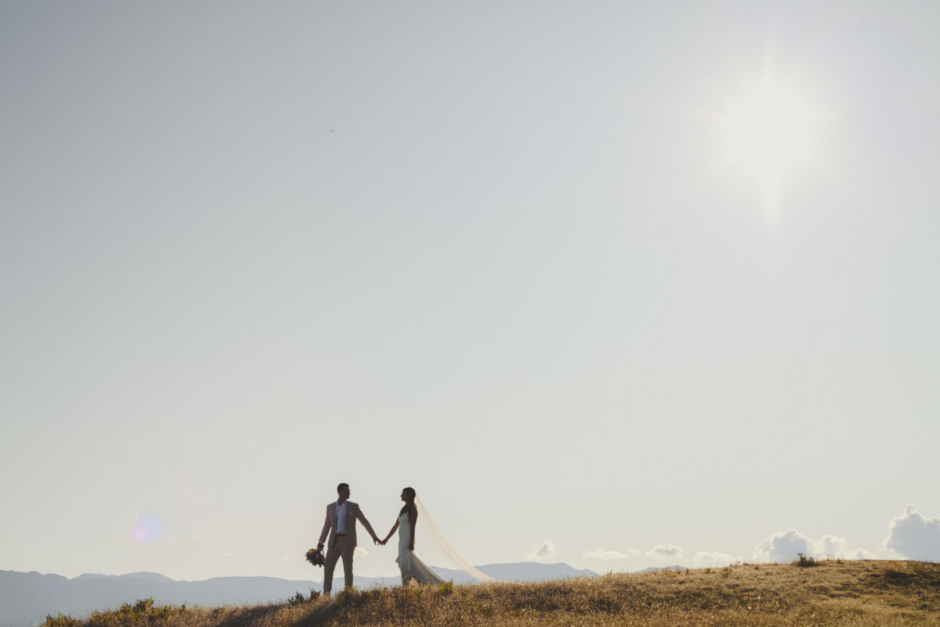 bride and groom walking along grassy cliffs with big sky behind them