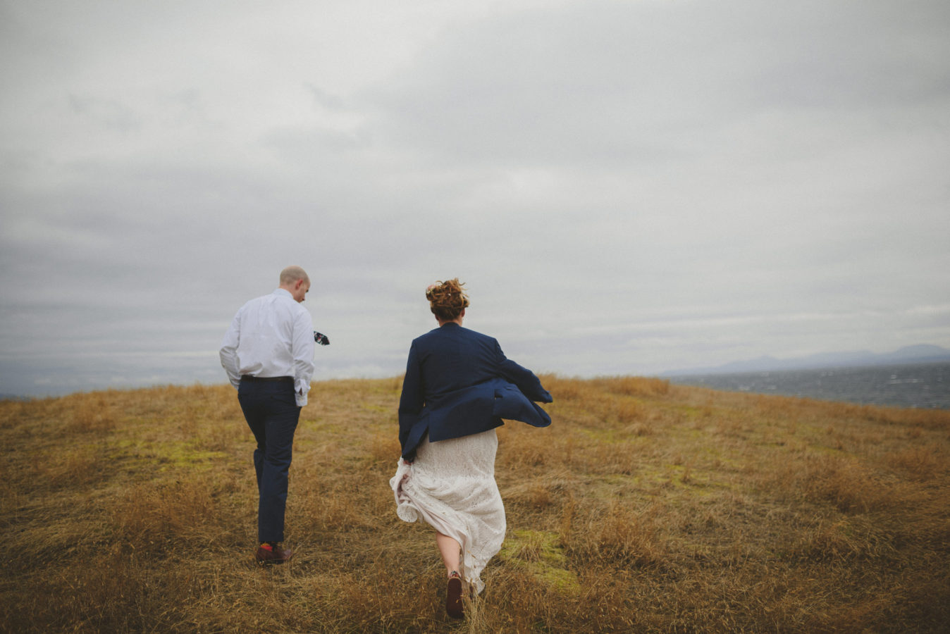 bride and groom walking on a grassy cliff in the wind