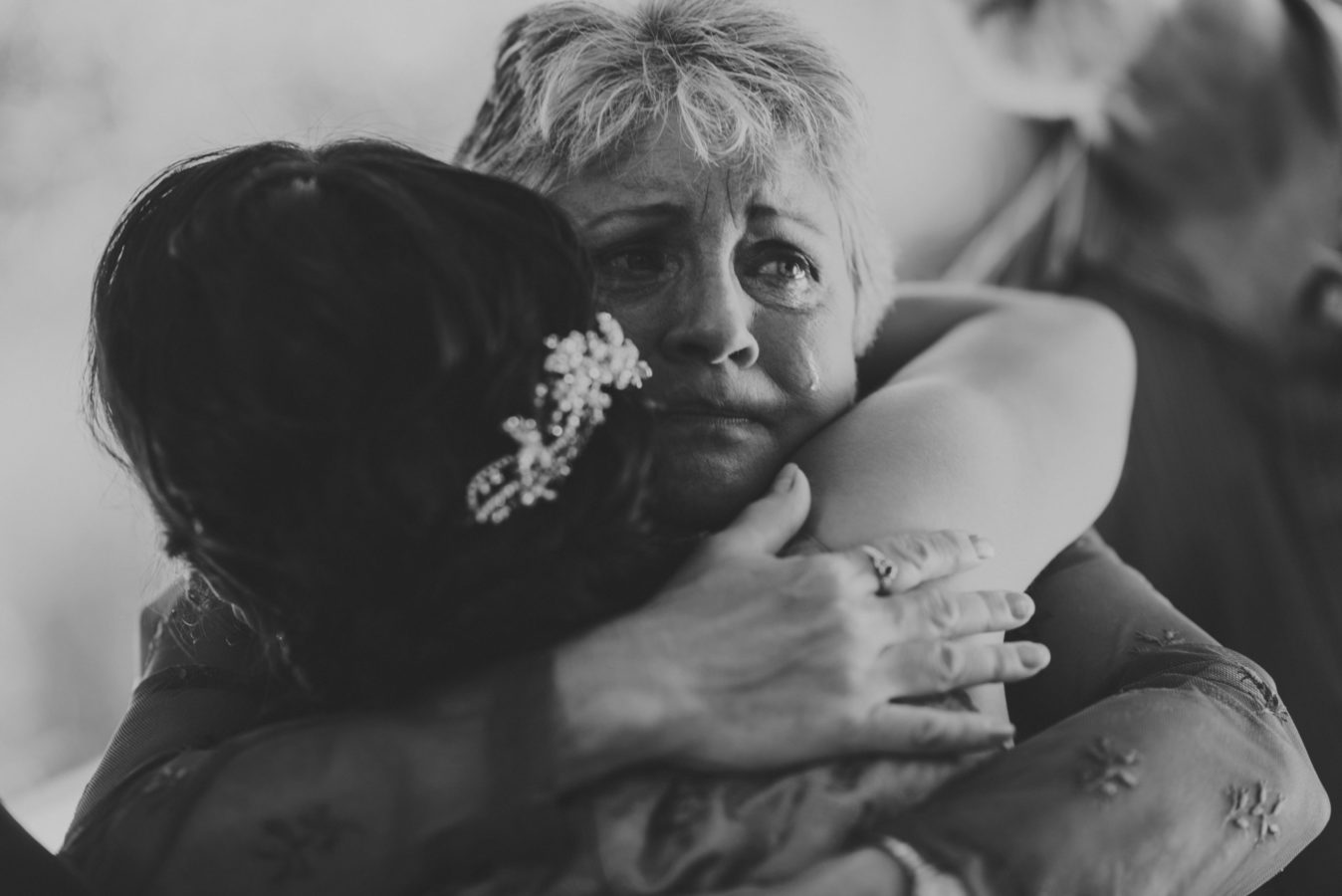 close up of a woman's teary face as she hugs a bride on her wedding day