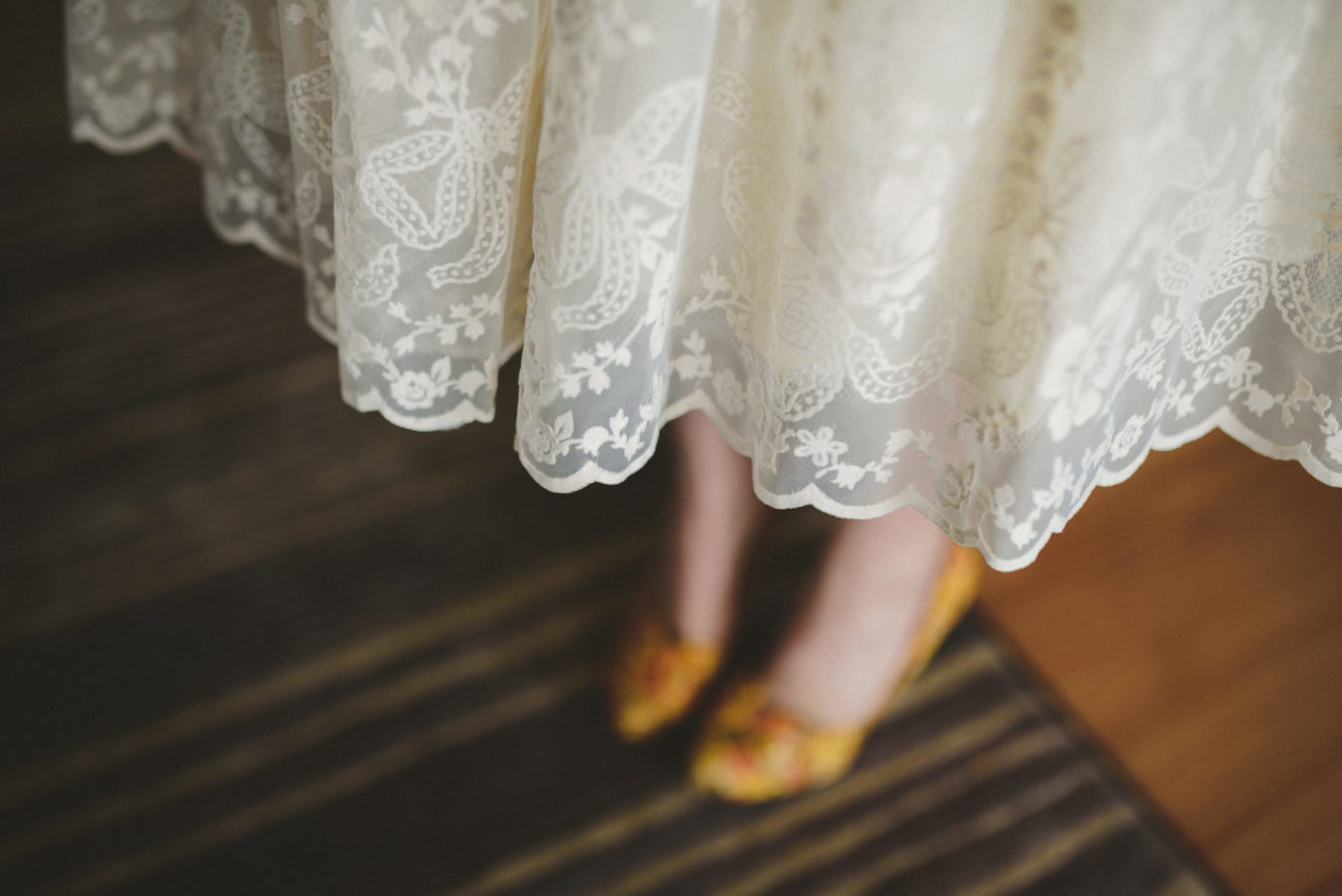 looking down on the lacy hem of a brides wedding dress with her yellow shoes underneath