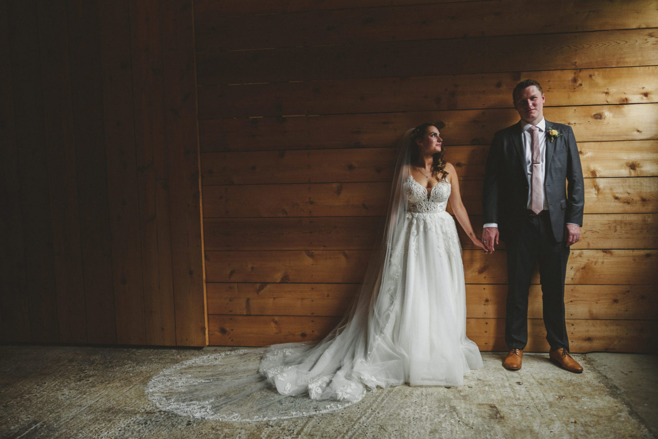 bride and groom holding hands in a barn with light coming in from the doors beside them