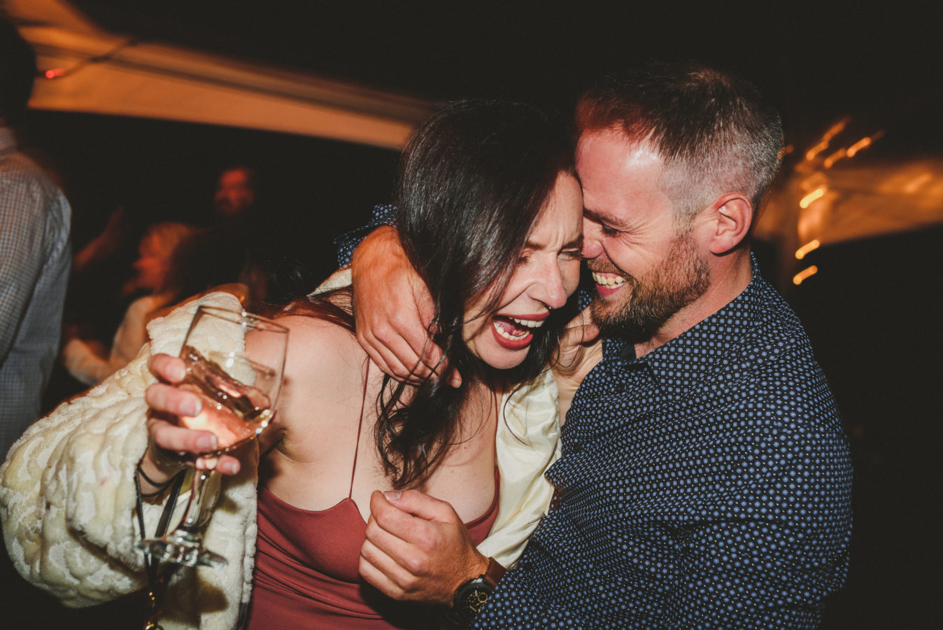 couple laughing & hugging while drinking and dancing on the dance floor at a wedding