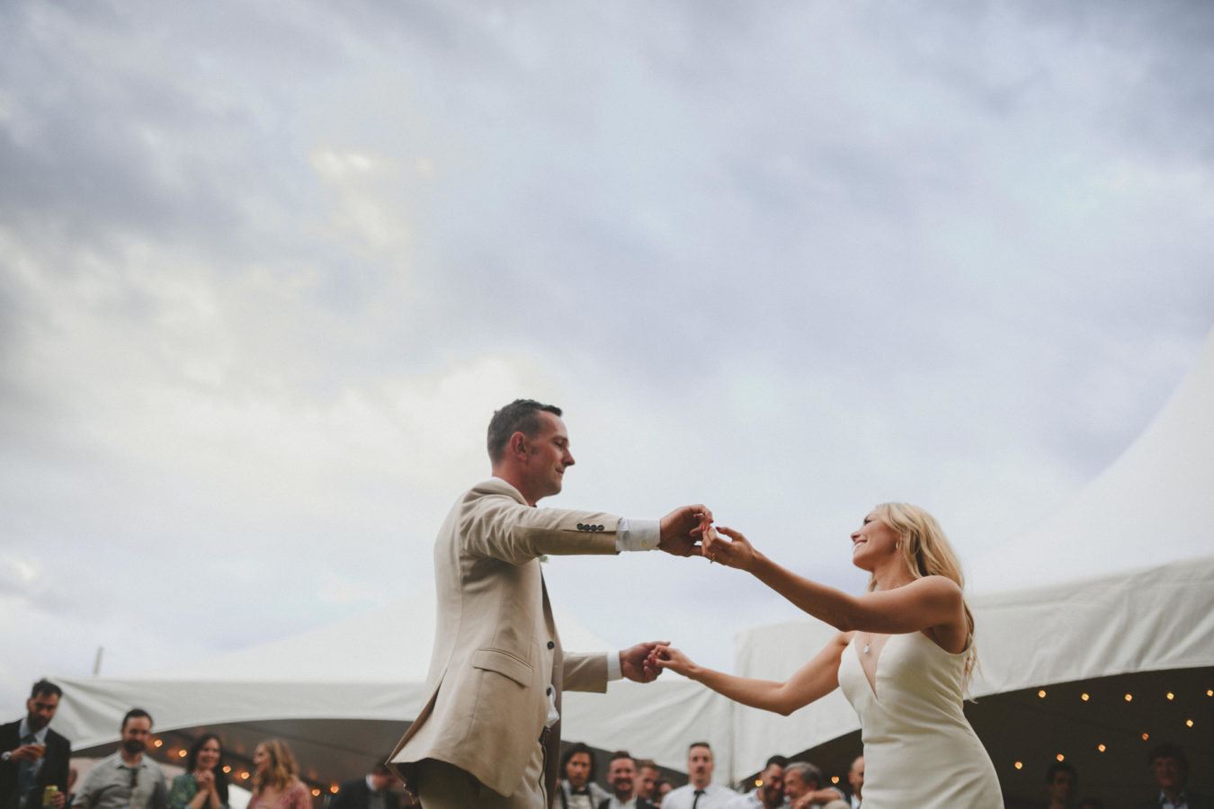 bride and groom dancing with guests looking on & white tents in the background