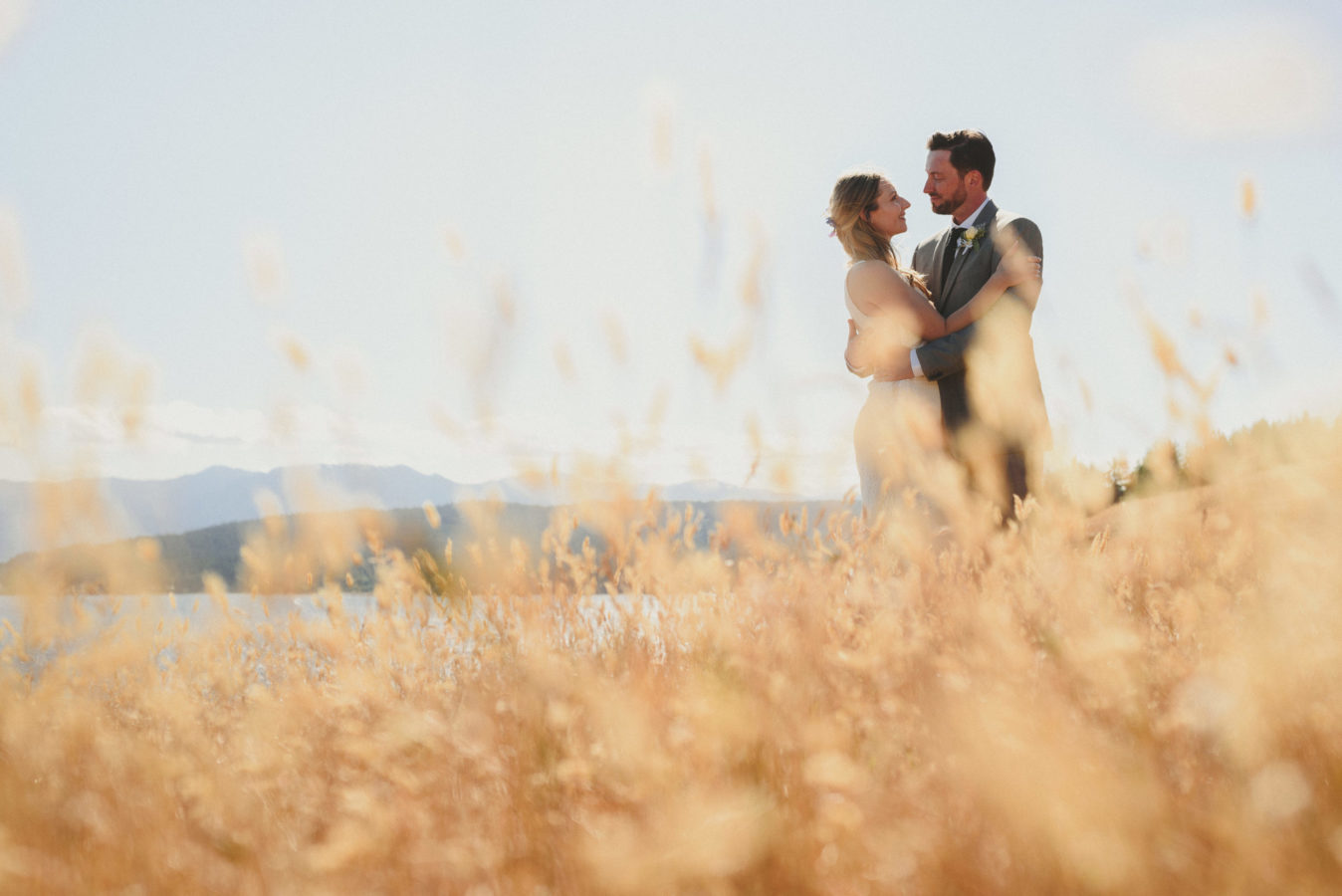 bride and groom embracing amongst the tall grass in a bluff overlooking the ocean