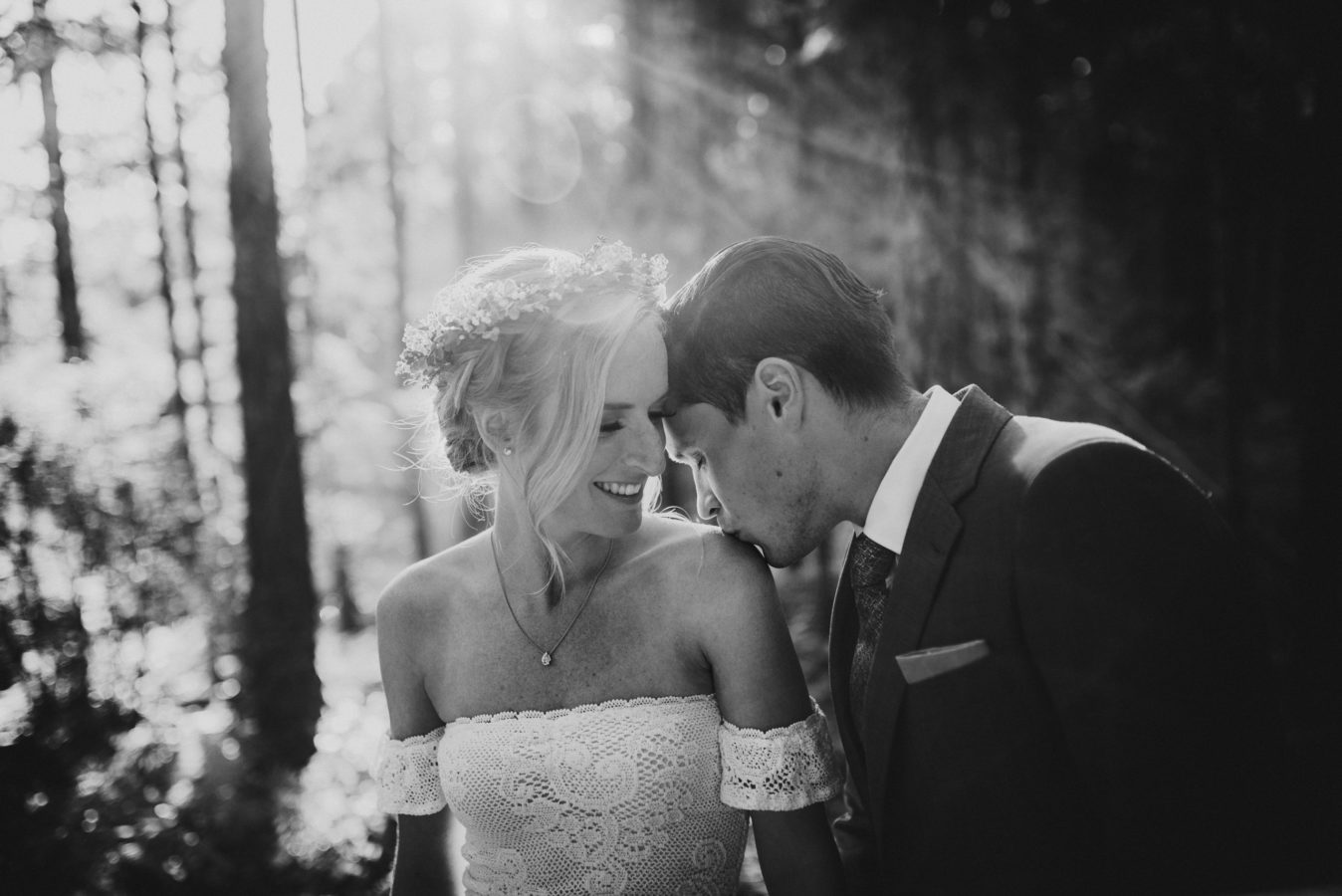 groom kissing his bride's shoulder in the sunlit forest on their wedding day