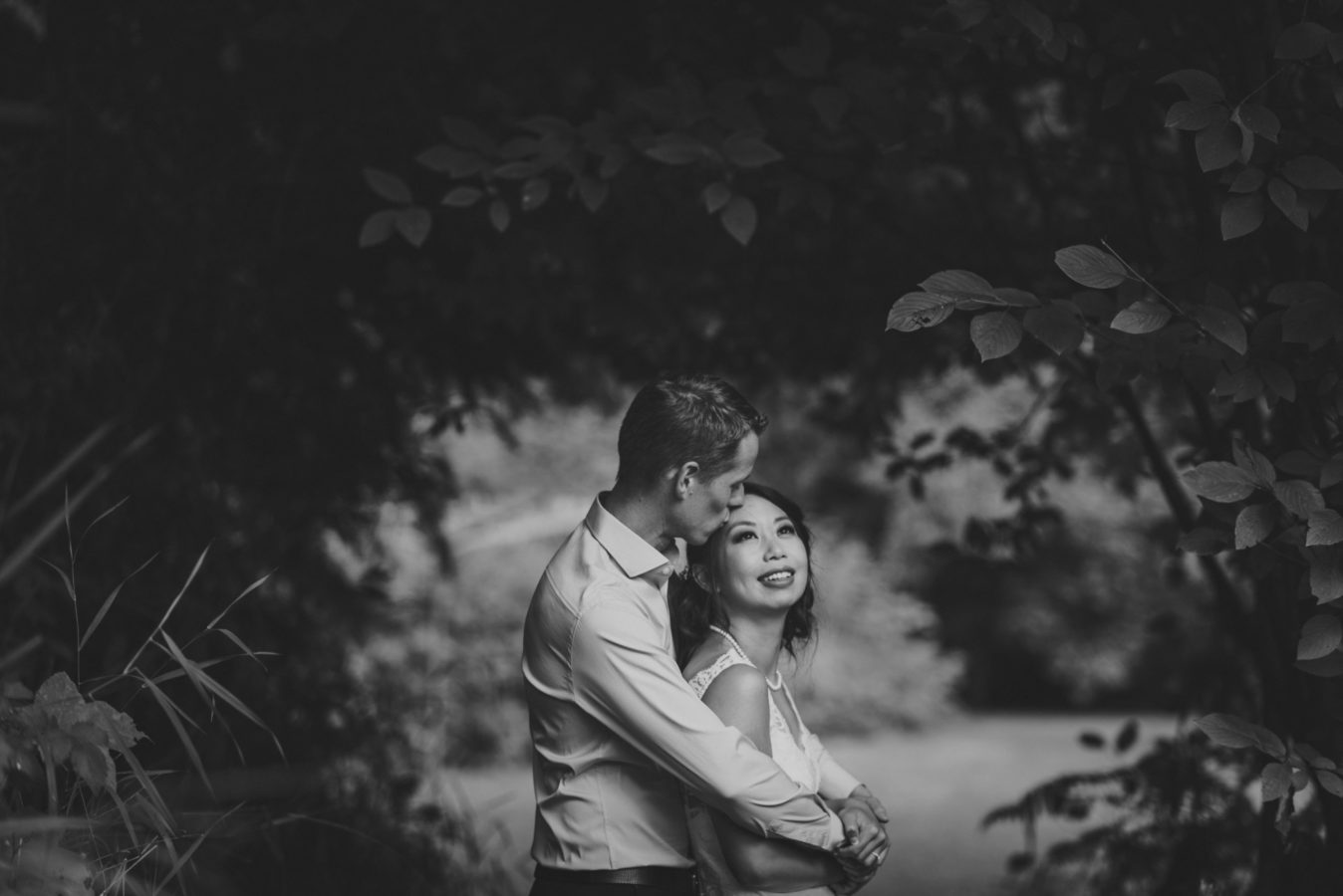 groom hugging his bride on their wedding day framed by trees and bushes