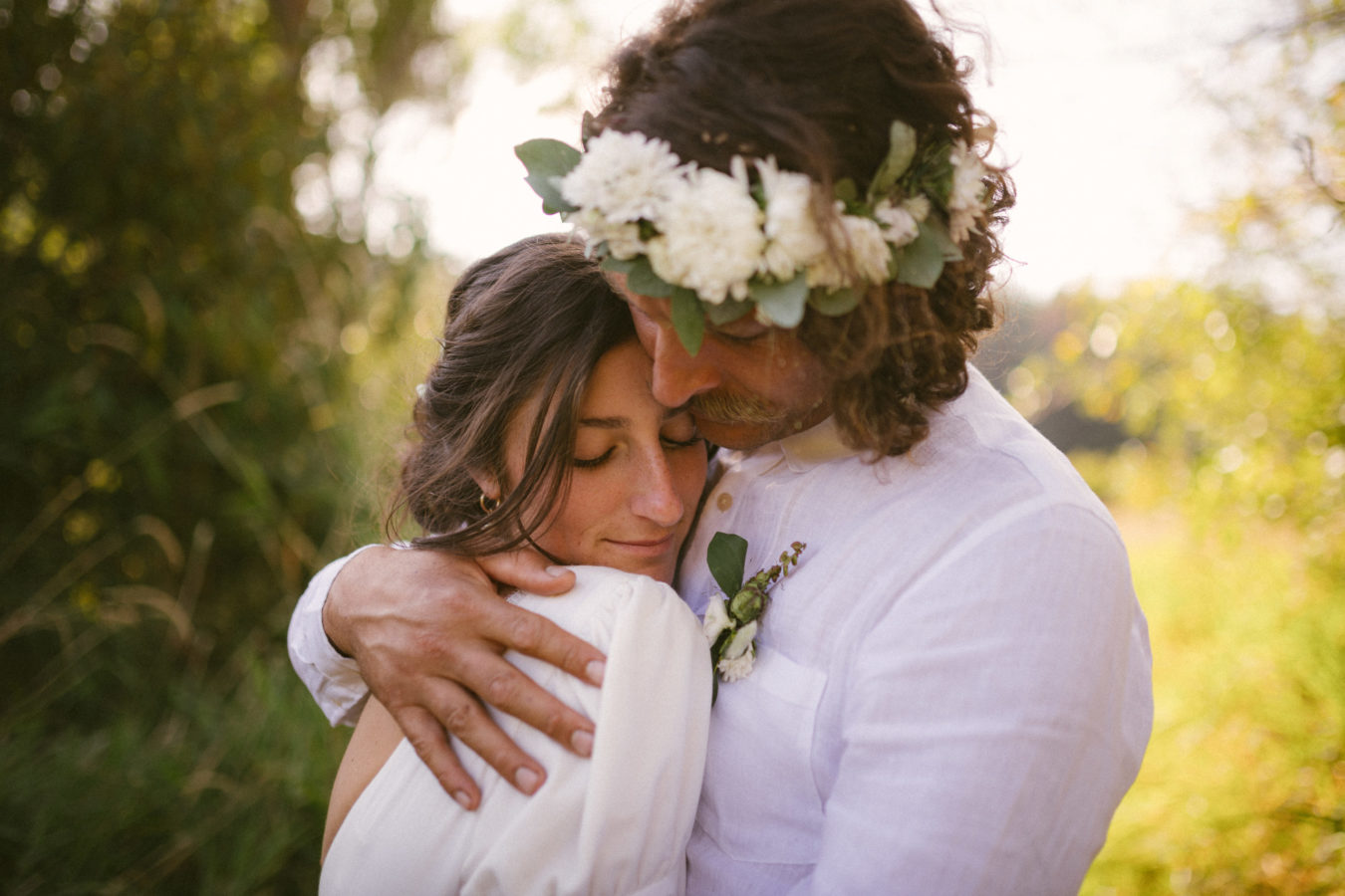 close up of a bride and groom intimately hugging on their wedding day with out of focus trees behind them