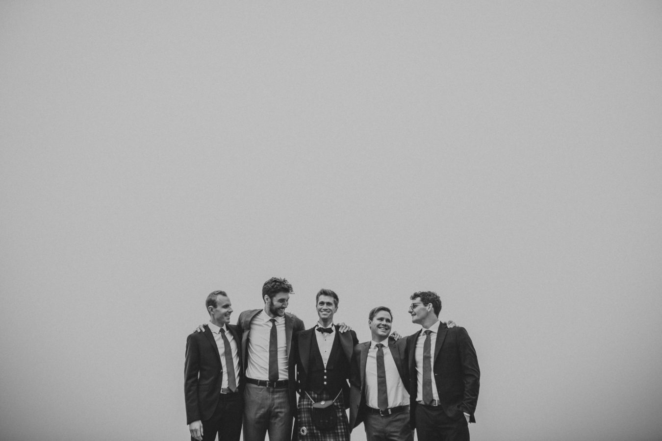 groom in a kilt with 4 groomsmen standing and laughing with a big foggy sky framing them