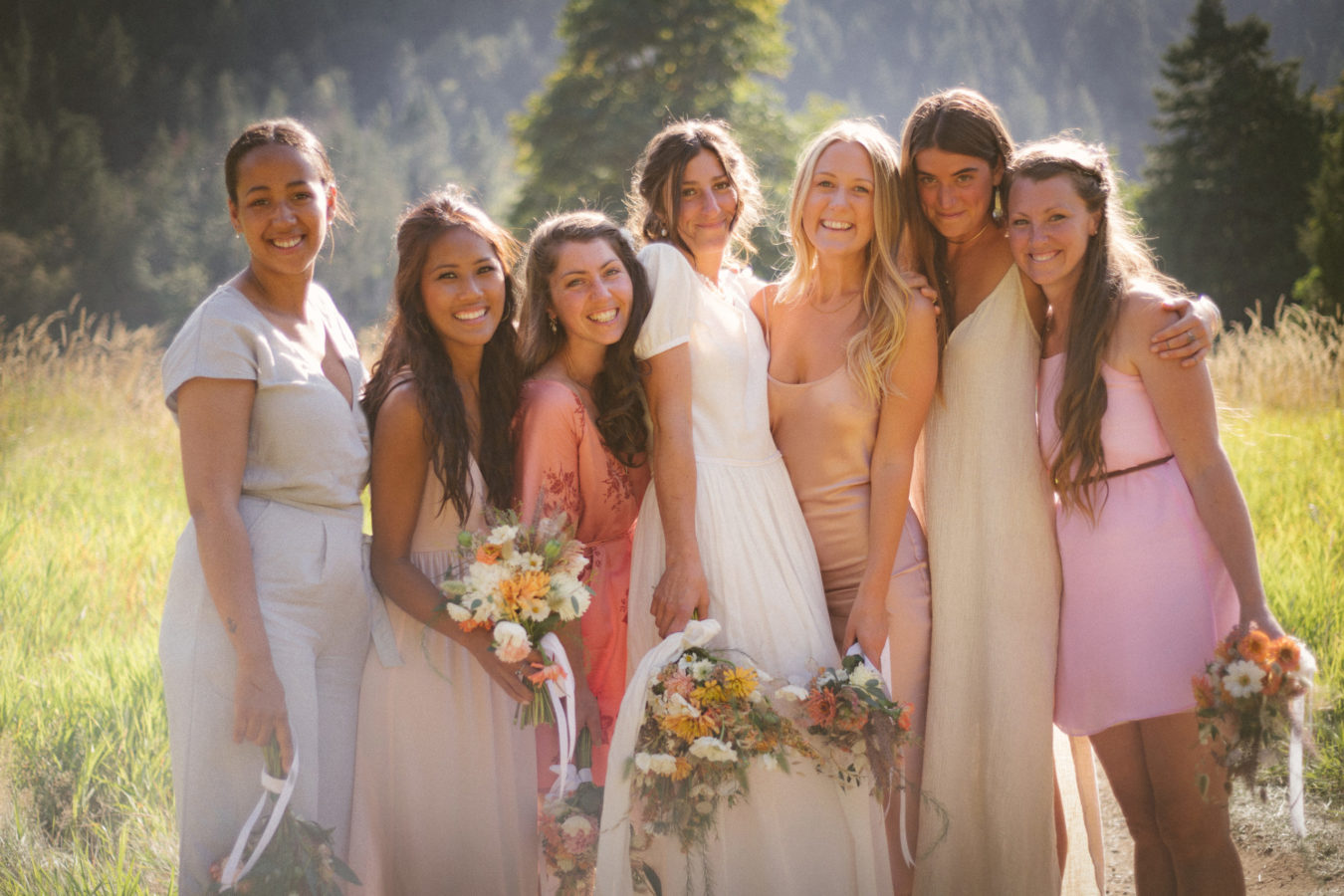 mixed race group of bridesmaids and bride standing in a field smiling and laughing with the sun shining behind them